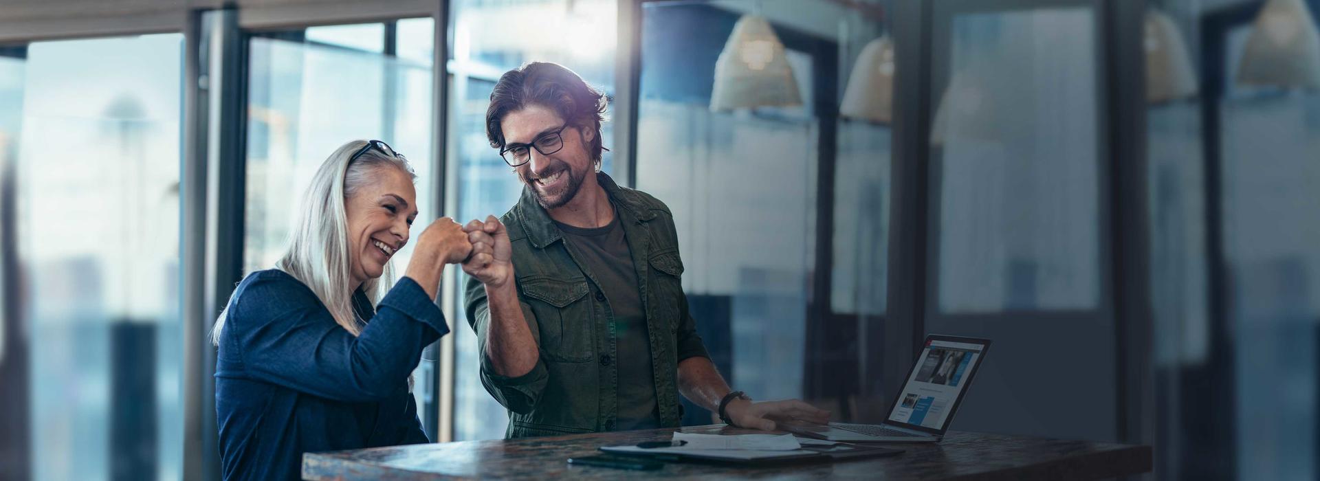 SCIPO ist digitaler Arbeitsplatz für Mitarbeiter, Geschäftspartner und Kunden. Zwei Mitarbeiter stehen an ihrem Arbeitsplatz und sind glücklich über ihren Projekterfolg.